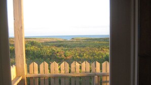 Une terrasse en bois, bordée d’une clôture blanche à piquets, qui offre une vue sur un paysage côtier.