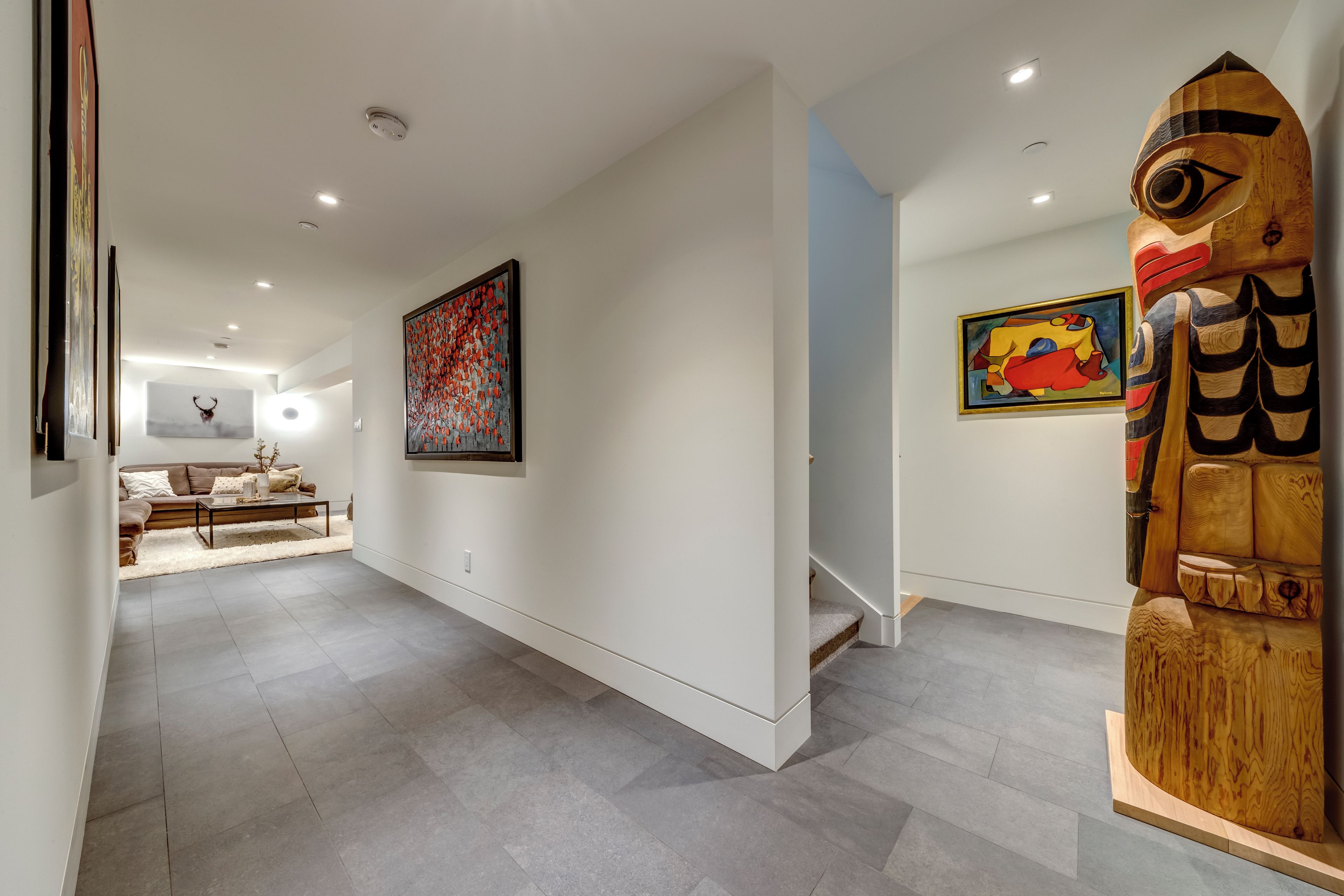 A modern interior with a staircase, a wooden sculpture, and two paintings on the walls.