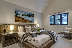 A bedroom with a large bed, a painting above the bed, a window with a view of snow-covered trees, and a chair. - Pinnacle Ridge 3 - Ski in Ski out, 7 Bedrooms, Hot Tub, Sauna & Billiards (Whistler)