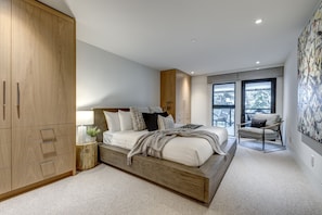 A modern bedroom with a large bed, wooden wardrobe, and a view of the outdoors through a window. - Pinnacle Ridge 3 - Ski in Ski out, 7 Bedrooms, Hot Tub, Sauna & Billiards (Whistler)