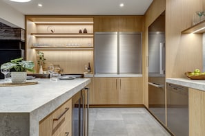 A modern kitchen with wooden cabinets, a stainless steel refrigerator, and a marble countertop.