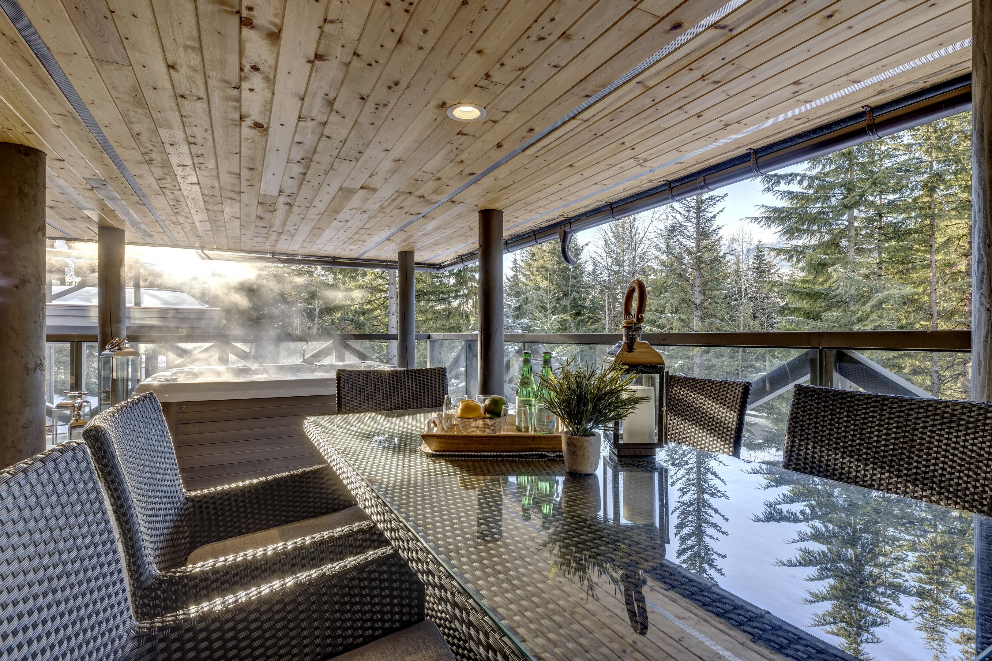 A spacious indoor area with a glass table, wicker furniture, and a view of a forest.