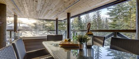A spacious indoor area with a glass table, wicker furniture, and a view of a forest.