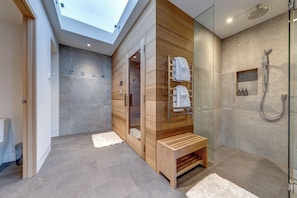 A modern bathroom with a skylight, a glass-enclosed shower, and a wooden bench. - This is the largest ski in ski out rental townhome in Whistler. And it's swanky. (Whistler)