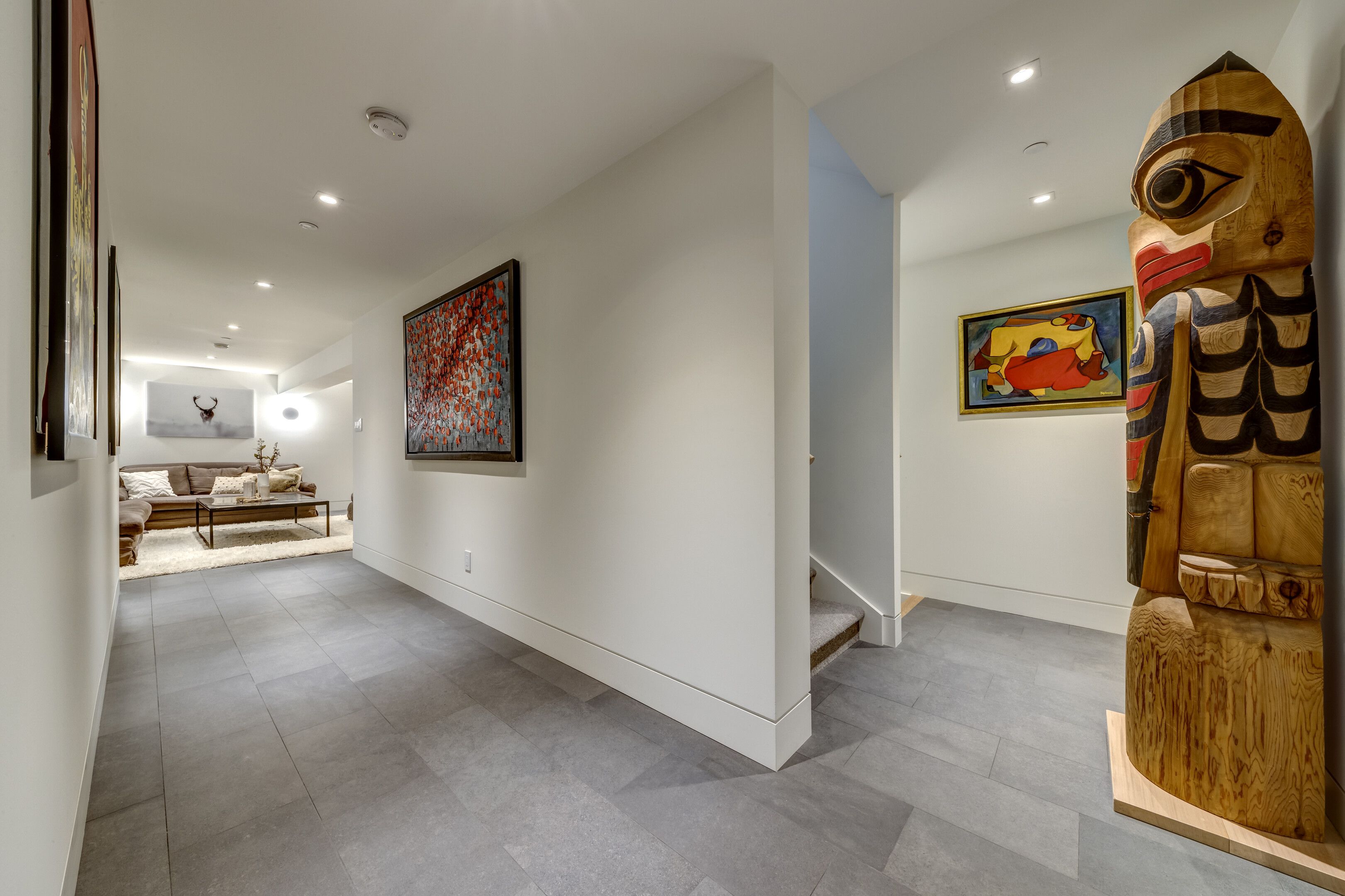 A modern interior with a hallway leading to a living area, a staircase, and a wooden sculpture.