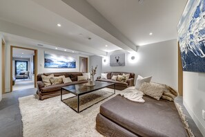 A modern living room with a brown sofa set, a coffee table, and a large painting of a mountain landscape. - Pinnacle Ridge 3 - Ski in Ski out, 7 Bedrooms, Hot Tub, Sauna & Billiards (Whistler)
