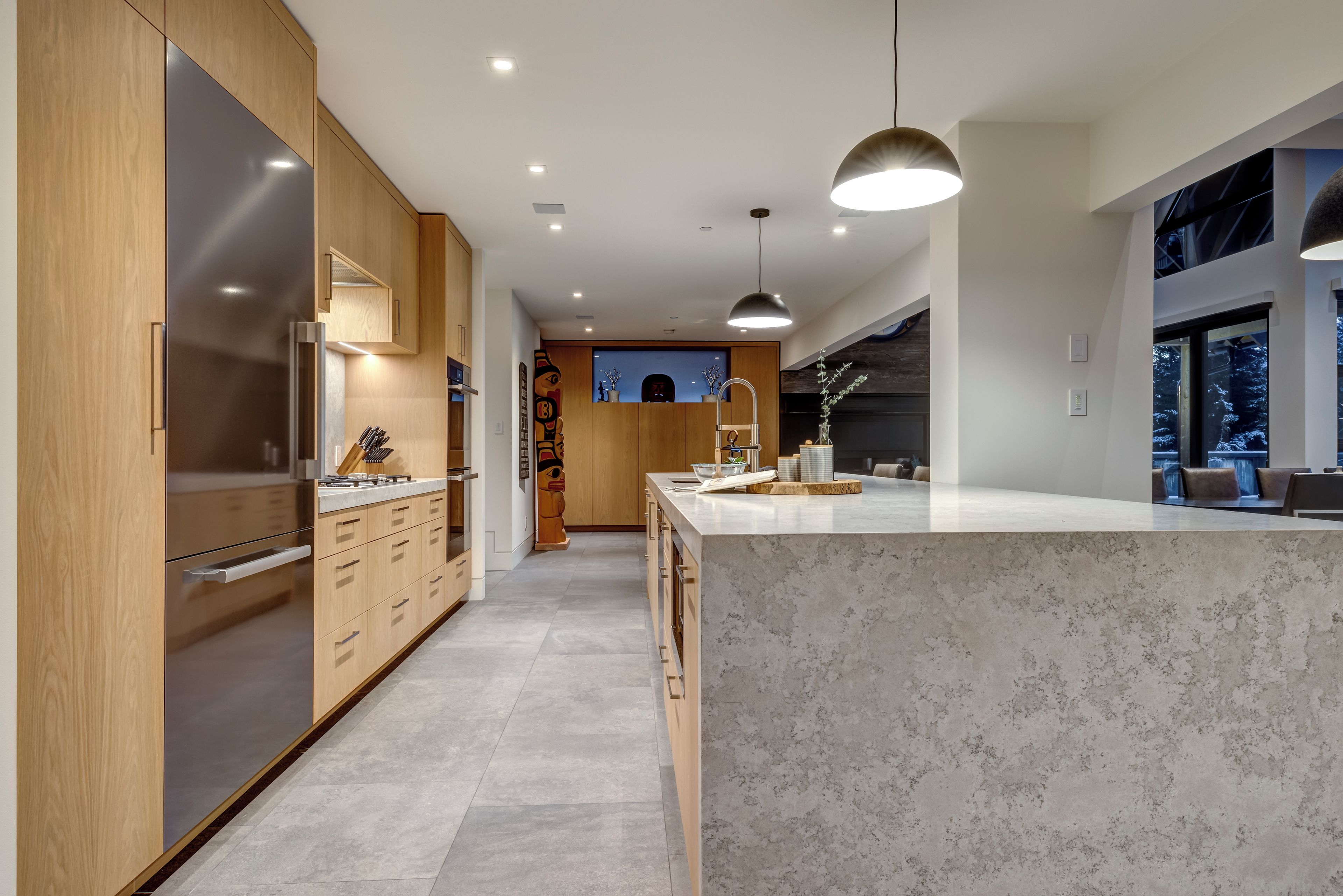 Een moderne keuken met houten kastjes, een marmeren eiland en hangende lampen.