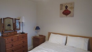 Een slaapkamer met een houten dressoir, twee bedlampen, een bed met witte lakens, en een kunstwerk aan de muur.