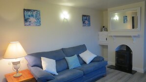Een woonkamer met een blauwe bank, een tafellamp en kunstwerken aan de muur.