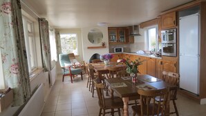 Een keuken met houten kastjes, een eettafel met stoelen, een magnetron, een oven en een koelkast.