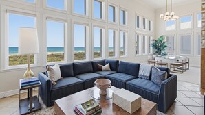 A spacious living area with a large sectional sofa, a coffee table, and a view of the ocean through large windows. - Manu Kai - Beachfront House With Private Pool And Hot Tub 6 Bedroom Home by RedAwning (South Padre Island)