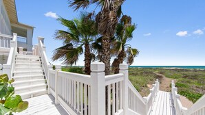 A wooden deck with white railings, leading to a beach with palm trees and a clear blue sky. - Manu Kai - Beachfront House With Private Pool And Hot Tub 6 Bedroom Home by RedAwning (South Padre Island)