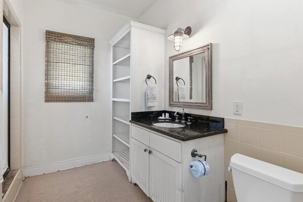 A bathroom with a white vanity, a sink, a toilet, a mirror, and a towel rack.