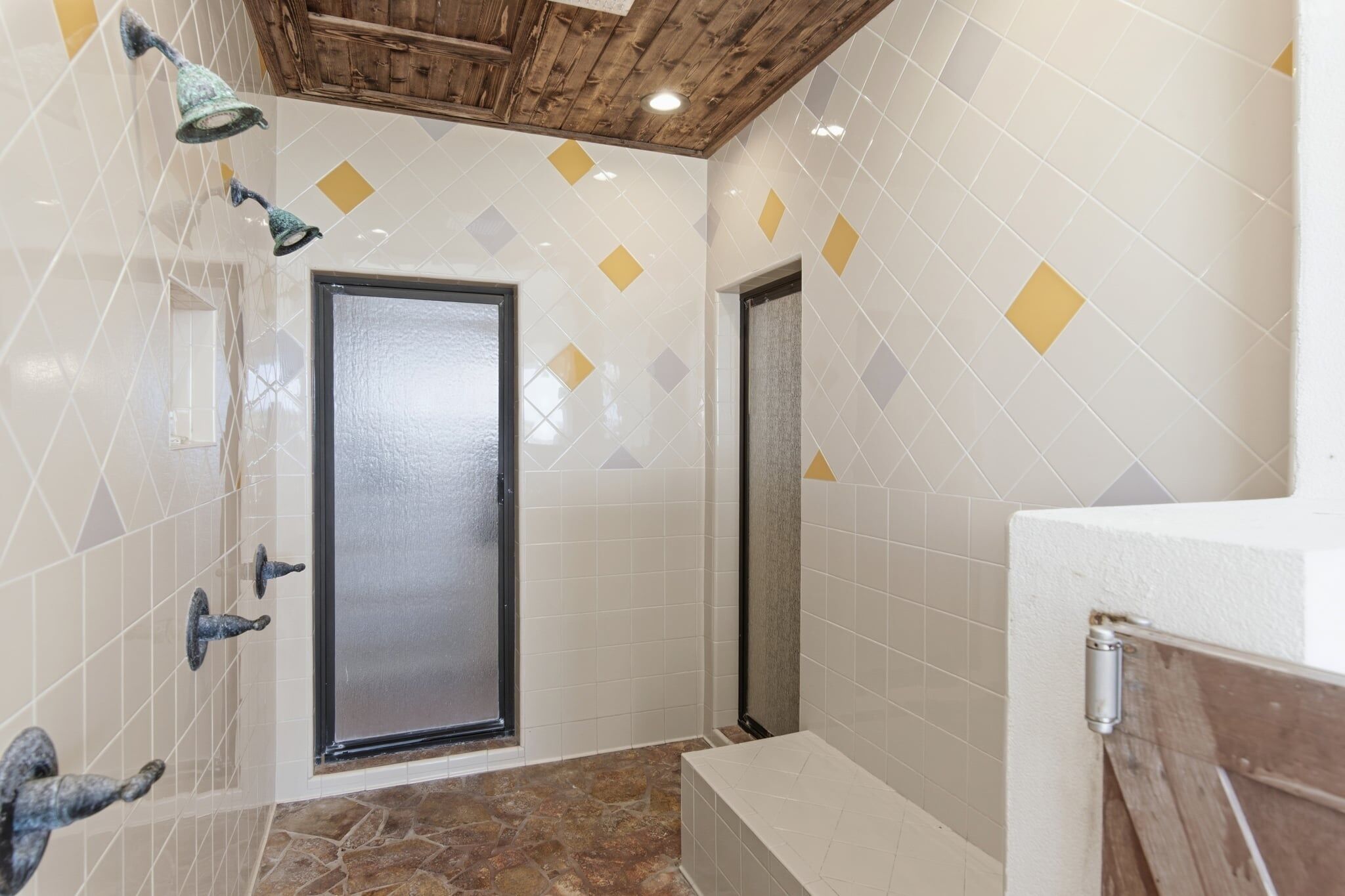 A bathroom with white tiled walls, a wooden ceiling, and a shower area.