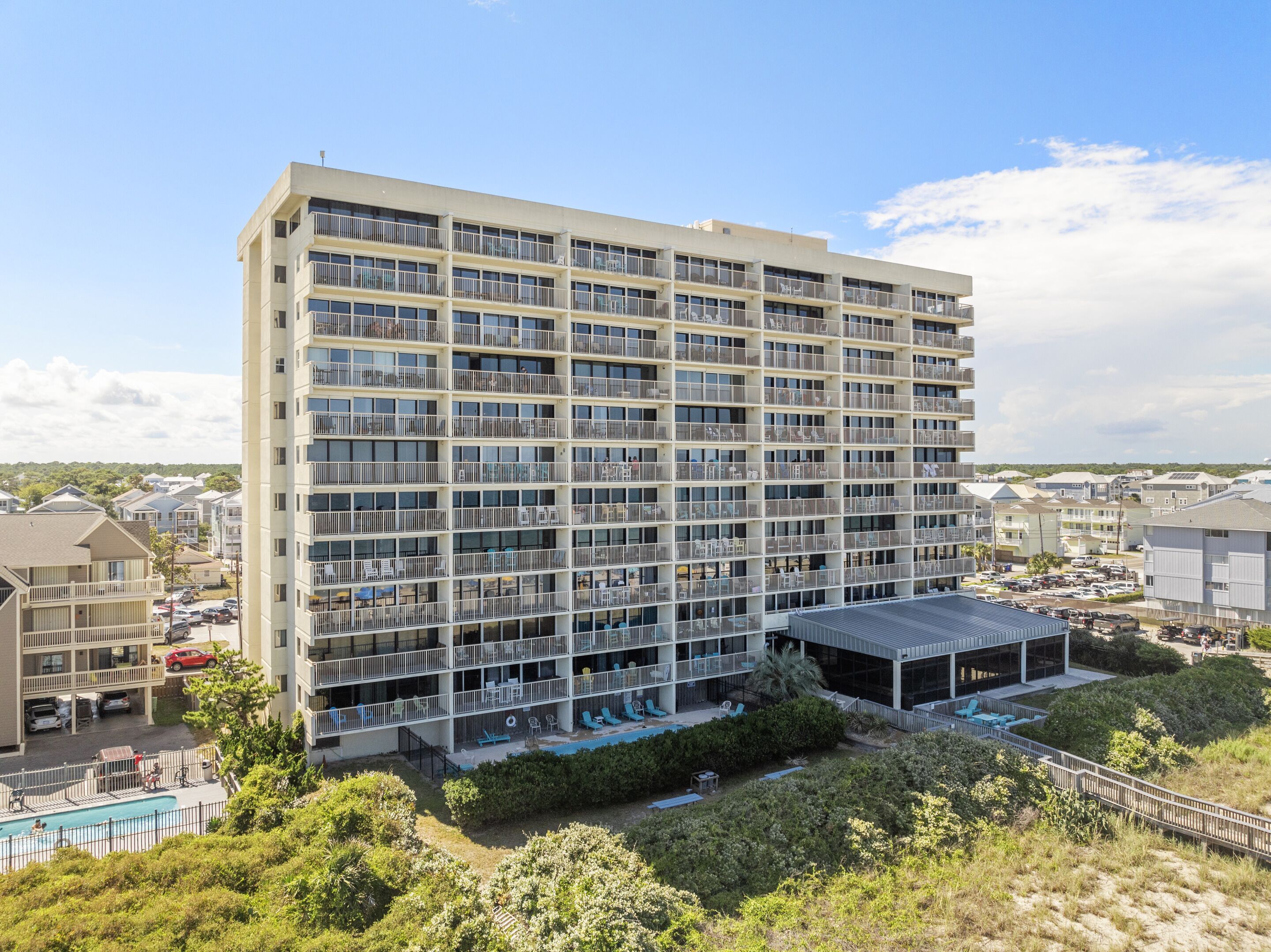 A multi-story hotel with balconies, a pool area, and a covered outdoor seating area.