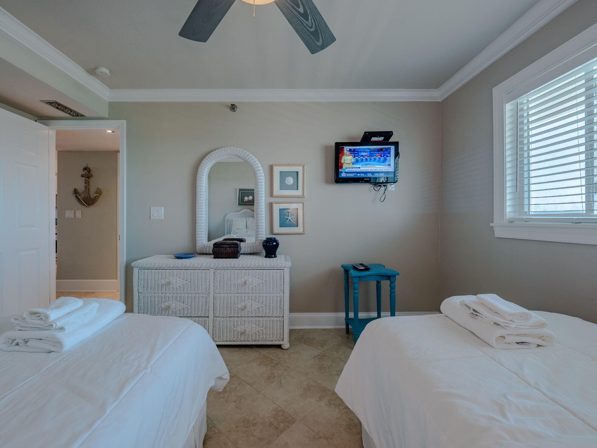 A bedroom with two beds, a television, a dresser, and a window with blinds.
