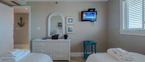 A bedroom with two beds, a television, a dresser, and a window with blinds.