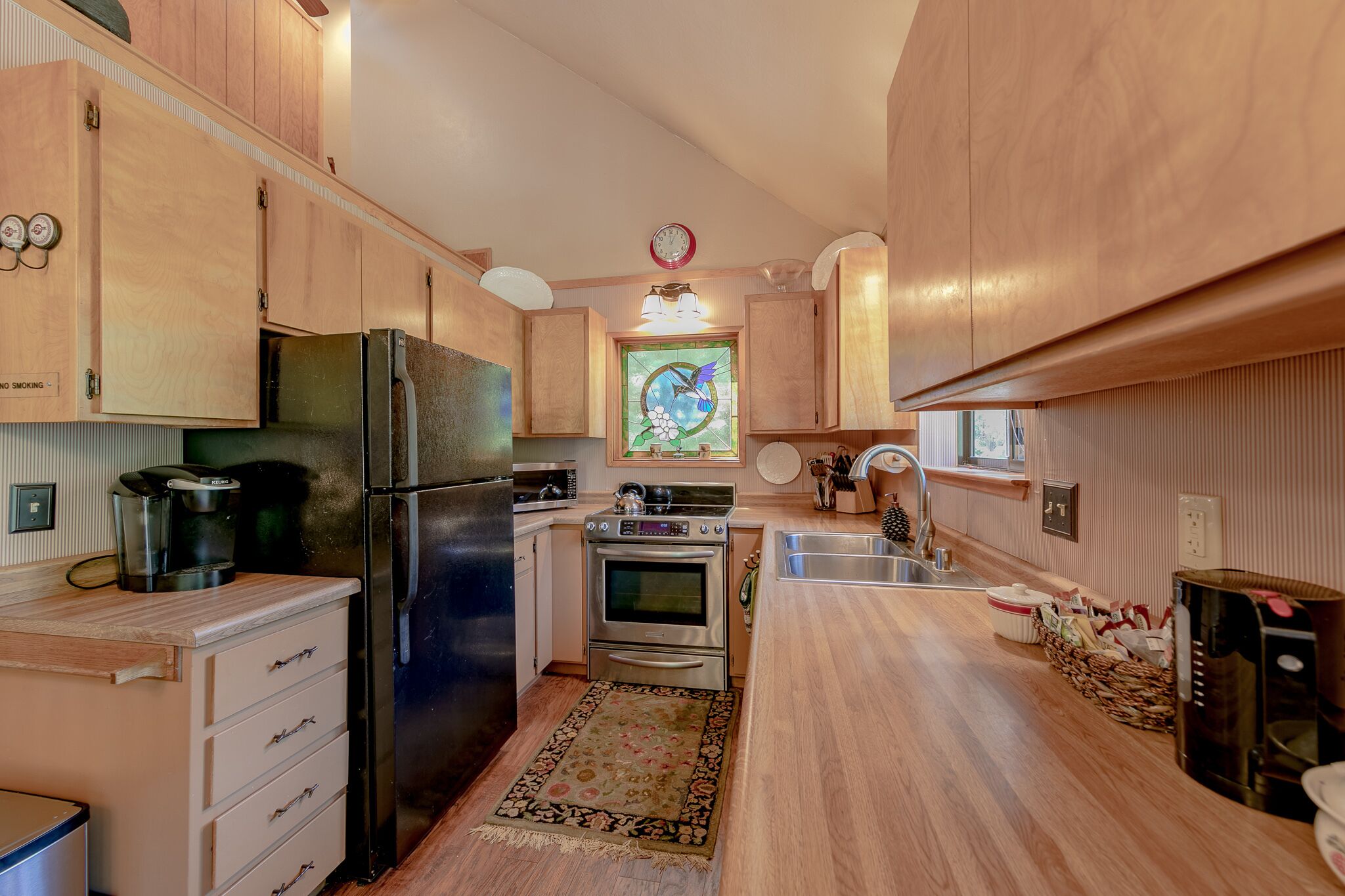 Une cuisine avec des meubles de rangement en bois, un réfrigérateur, un four, un four à micro-ondes et une machine à café.
