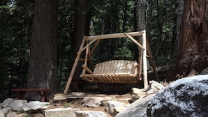 Un conjunto de columpios de madera en un área boscosa con rocas grandes y árboles.