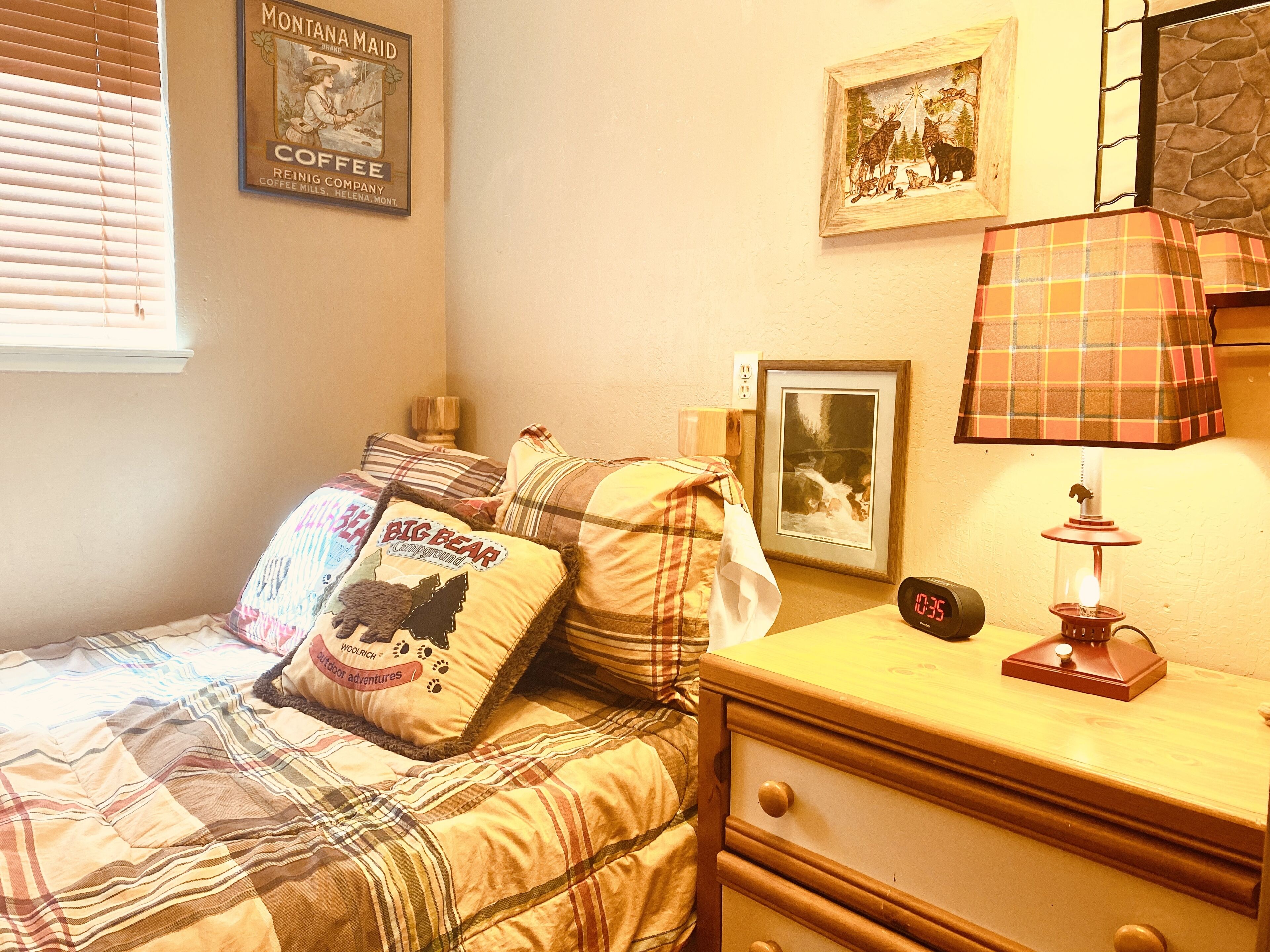 Een slaapkamer met een bed, nachtkastje, lamp, een ingelijst schilderij en een wandklok.