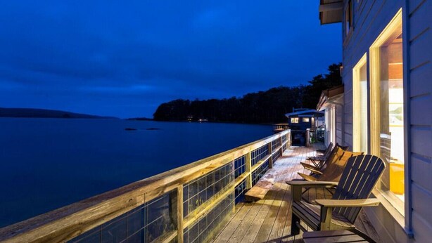 A wooden deck with a railing overlooking a body of water at dusk. - Bleu Bay | Charming Coastal Cottage, Private Beach (Marshall)