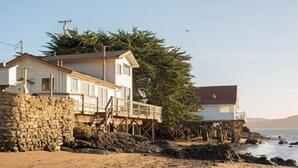A coastal house with a stone foundation, wooden deck, and a view of the ocean. - Bleu Bay | Charming Coastal Cottage, Private Beach (Marshall)