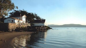 A coastal house with a wooden pier extending into calm waters, surrounded by trees and a clear sky. - Bleu Bay | Charming Coastal Cottage, Private Beach (Marshall)