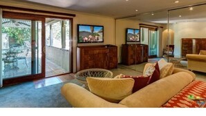 A spacious living room with a sofa, a television, and a glass door leading to an outdoor area. - Palm Springs Paradise (Palm Springs)