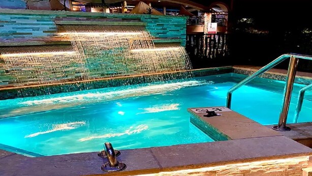 Une piscine agrémentée d’une cascade, d’un jacuzzi et d’un mur en pierre.