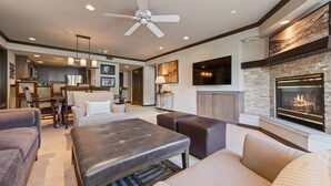 Un salon moderne avec une cheminée, un ventilateur de plafond et un téléviseur fixé au mur.