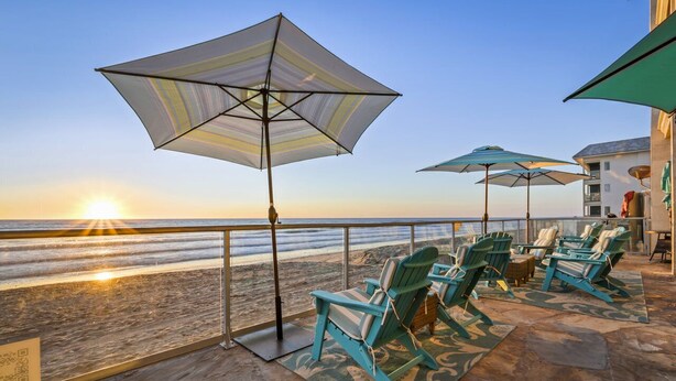 A beachside patio with Adirondack chairs and large umbrellas, overlooking the ocean. - 3 Bedroom Oceanfront Paradise! (Carlsbad)