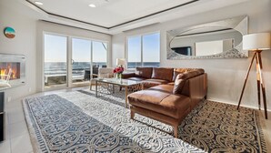 A modern living room with a leather sofa, a coffee table, and a large window offering a view of the ocean. - 3 Bedroom Oceanfront Paradise! (Carlsbad)