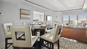 A modern dining area with a glass table, beige chairs, and a view of the ocean. - 3 Bedroom Oceanfront Paradise! (Carlsbad)