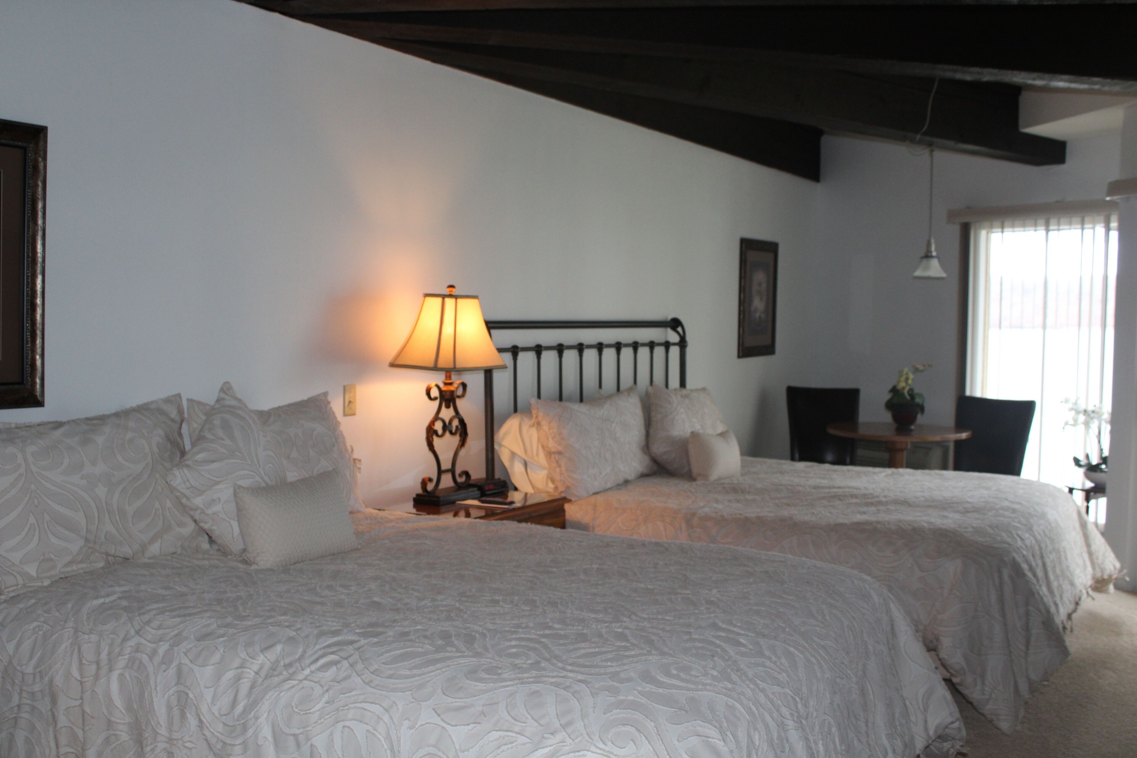 Un dormitorio con dos camas, una mesita de noche con lámpara, una silla y una pequeña mesa con una planta.