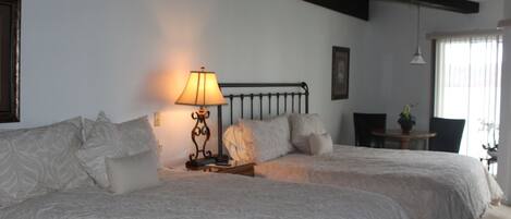 Un dormitorio con dos camas, una mesita de noche con lámpara, una silla y una pequeña mesa con una planta.