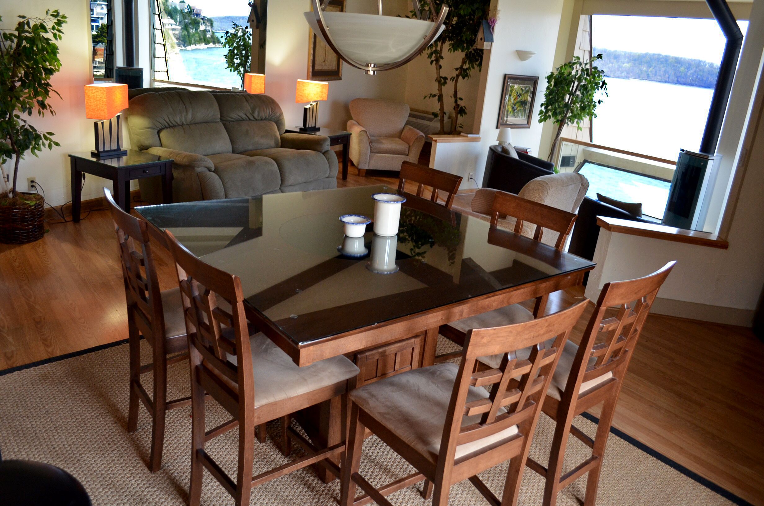 A dining area with a glass-top table surrounded by wooden chairs, a sofa, and two lamps.