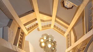 Un intérieur à plusieurs niveaux avec un escalier central, un luminaire au plafond et une affiche au niveau supérieur.
