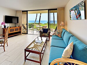 A living room with a sofa, coffee table, TV, and a view of the ocean.
