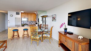 Una cocina moderna con armarios de madera, encimera de mármol y un comedor con sillas de mimbre y una mesa de vidrio.