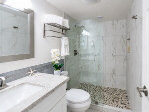 A modern bathroom with a glass shower enclosure, a marble-tiled shower floor, a white toilet, and a granite countertop with a sink.