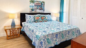 Une chambre à coucher avec un lit, deux lampes de chevet, un ventilateur de plafond, un tableau et une fenêtre avec des rideaux.