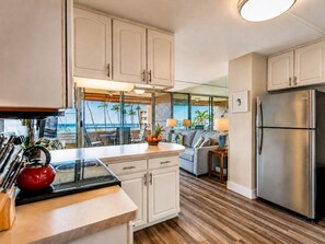 Una cocina con armarios blancos, un refrigerador de acero inoxidable y vistas al océano a través de amplios ventanales.