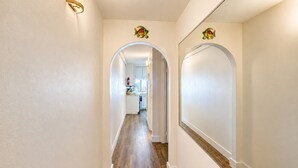 Un couloir aux murs blancs, doté d’un plancher en bois, et d’où l’on aperçoit une cuisine à travers une arche.
