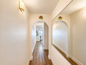 Un couloir aux murs blancs, doté d’un plancher en bois, et d’où l’on aperçoit une cuisine à travers une arche.