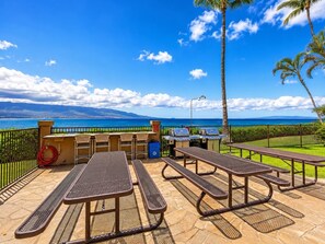 An outdoor patio with picnic tables and barbecue grills, overlooking a beach and ocean. - Tranquil Maalaea Oceanfront Condo Ocean and Haleakala Views Pool Near Harbor (Wailuku)