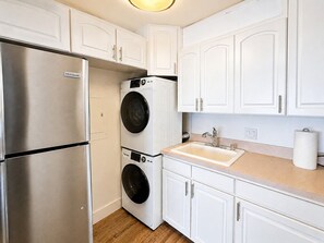 Une cuisine compacte dotée d’un réfrigérateur en acier inoxydable, d’un lave-linge à deux tambours, de meubles blancs, d’un évier et d’un plan de travail.