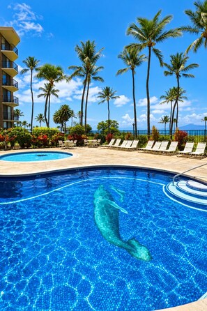 A swimming pool with a mermaid sculpture, surrounded by palm trees and lounge chairs, with a clear blue sky in the background. - Scenic Kihei Village by the Sea Renovated Condo Ocean Views Lanai Pool (Kihei)
