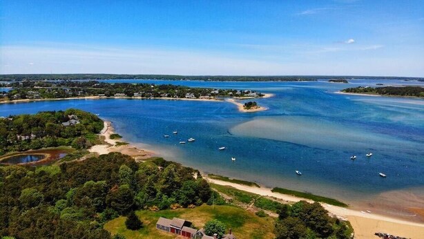 An aerial view of a coastal area with a beach, boats, and a small house.