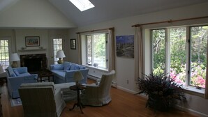 A spacious living room with a fireplace, comfortable seating, large windows, and a view of greenery.