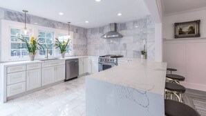 Una cucina moderna con mobili bianchi, un'isola in marmo ed elettrodomestici in acciaio inossidabile.